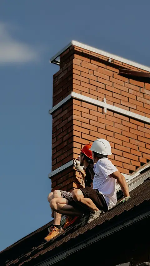 Roofers working beside a brick chimney